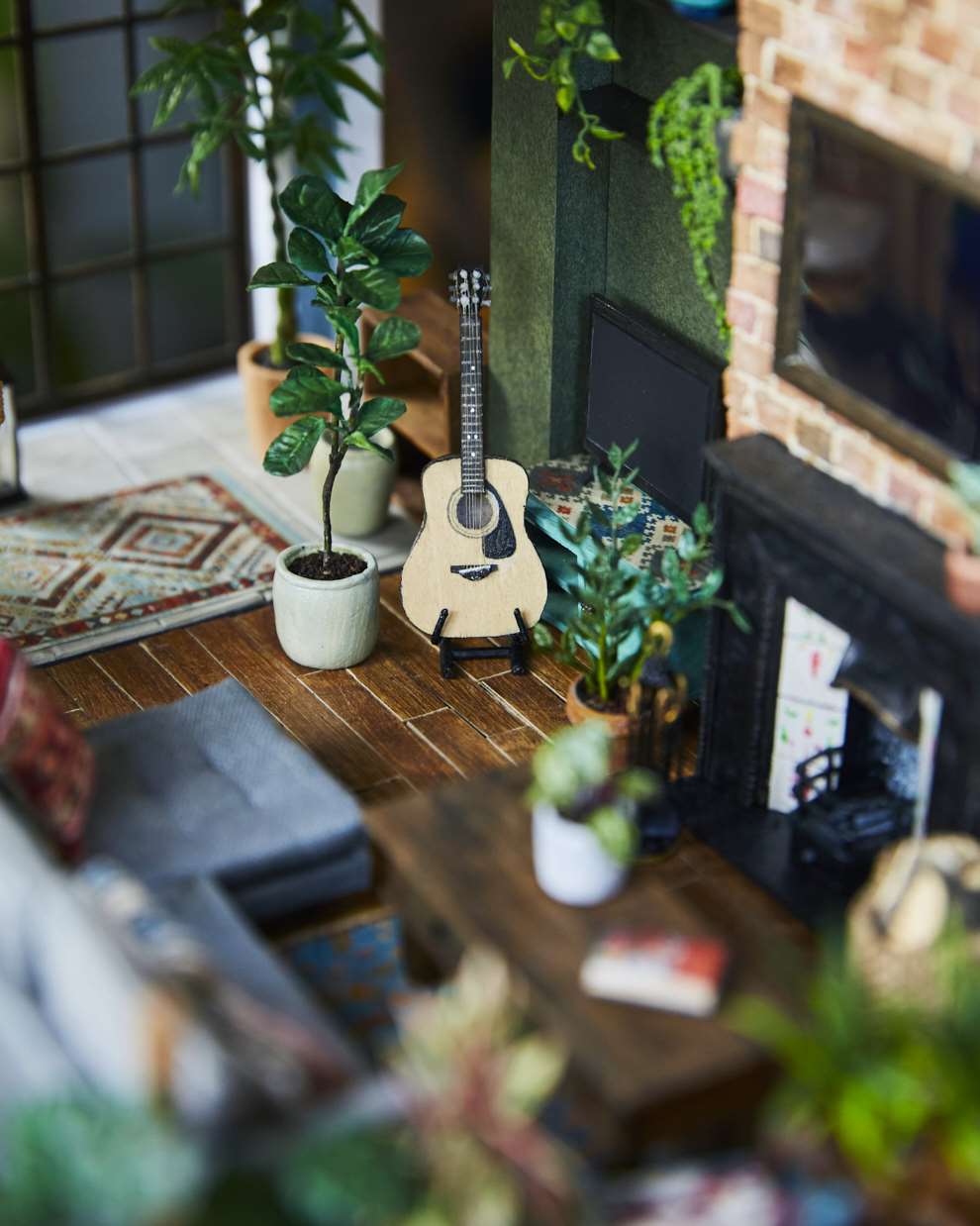 Hannah Lemon, Miniature detailed set design. Living room with a fireplace, guitar, TV, and coffee table surrounded by houseplants and botanicals. Tiny sculpture made from air drying clay, paper, wood, paint, mixed media. 