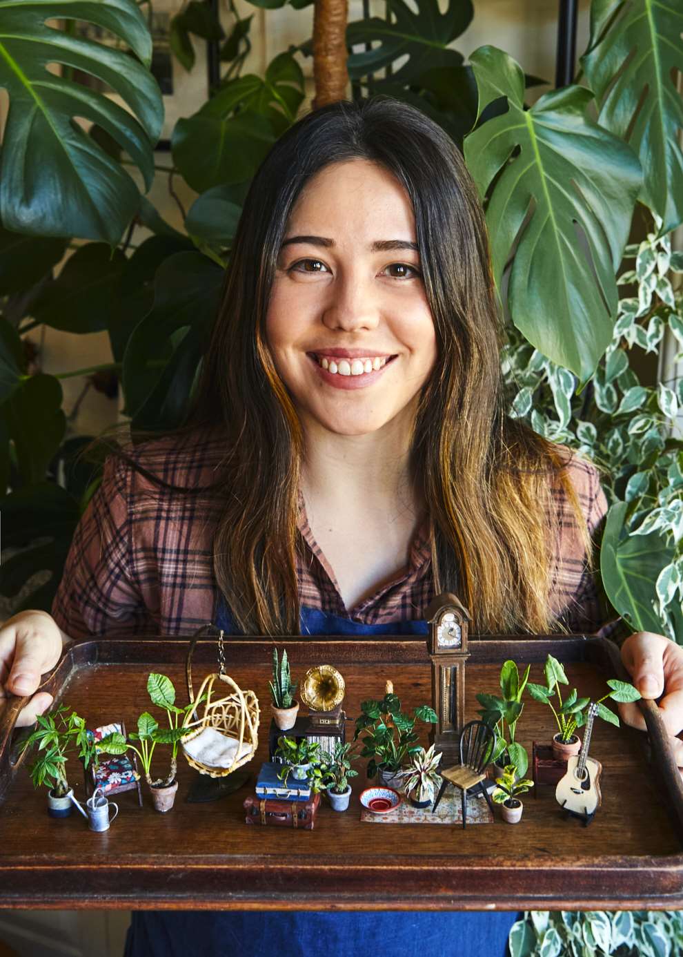 Hannah Lemon, Hannah Lemon holding wooden tray with series of tiny creations including houseplants, a clock, a table, a bookshelf and suitcase.  